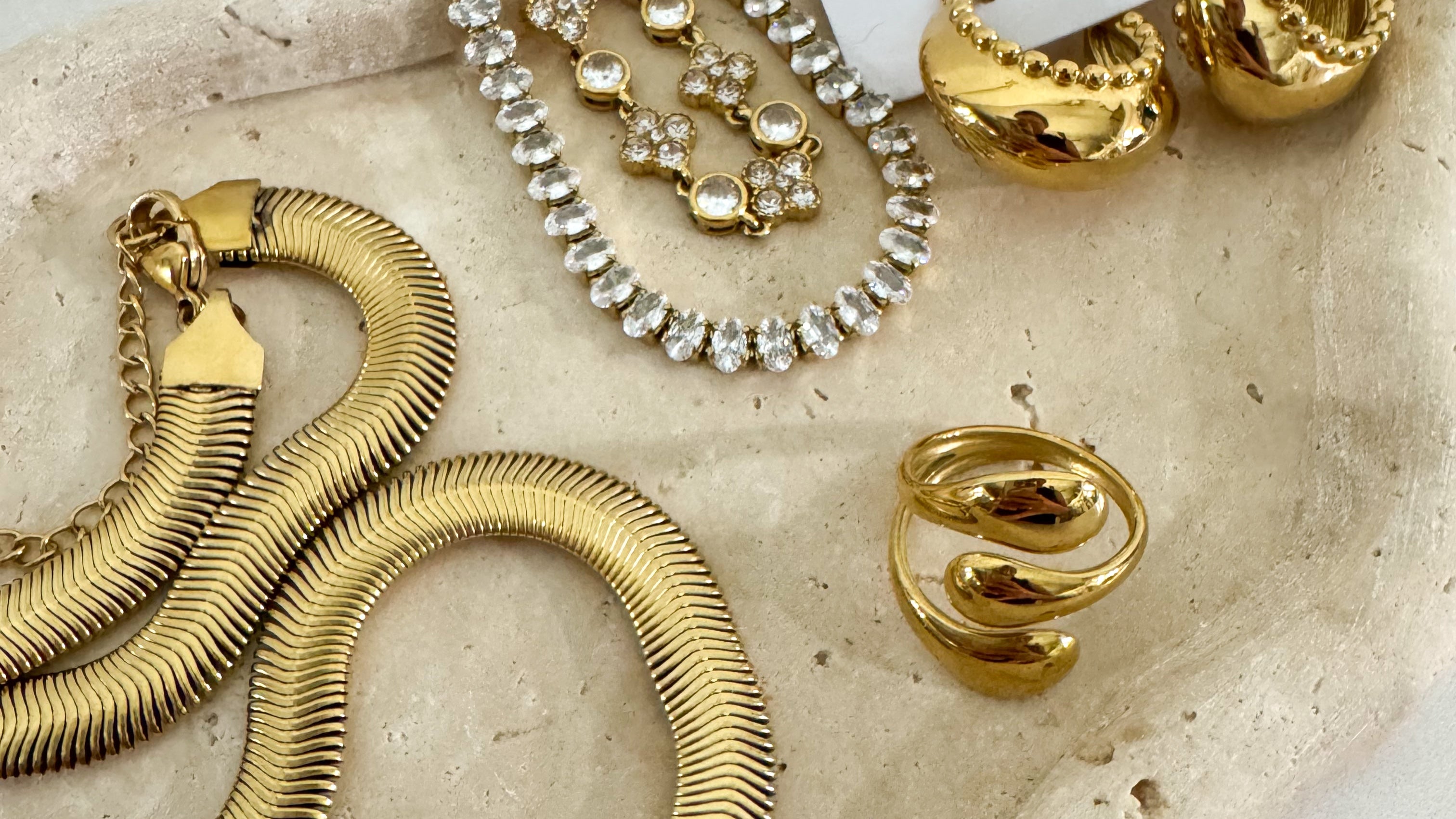 Gold jewelry including a necklace, bracelet, and hoop earrings on a stone surface with 'Savvy Bling' branding.