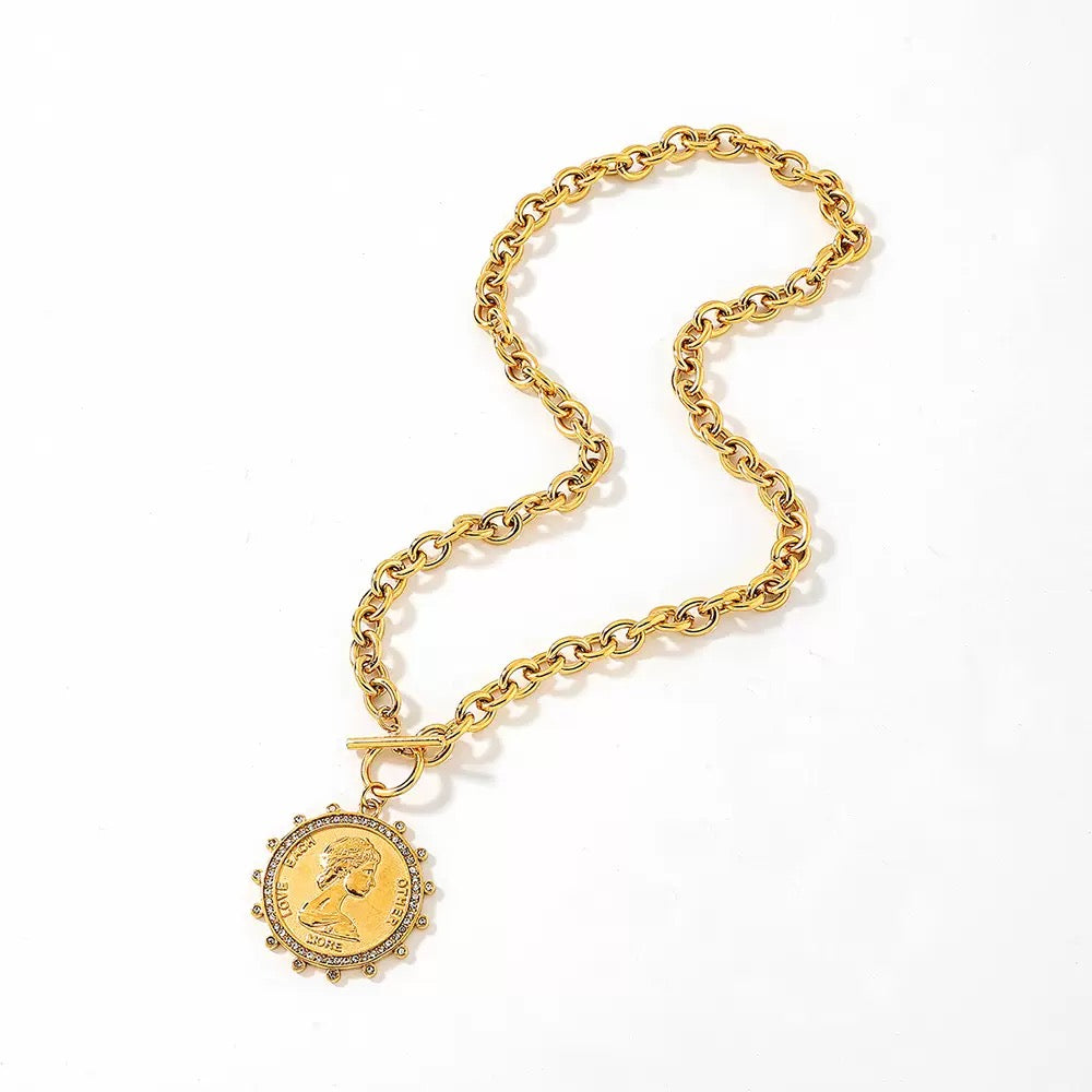 A gold chain necklace with a round medallion pendant featuring a profile portrait, photographed on a clean white background.