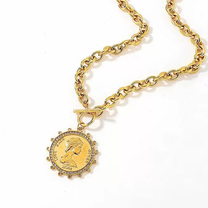 A gold chain necklace with a round medallion pendant featuring a profile portrait, photographed on a clean white background.